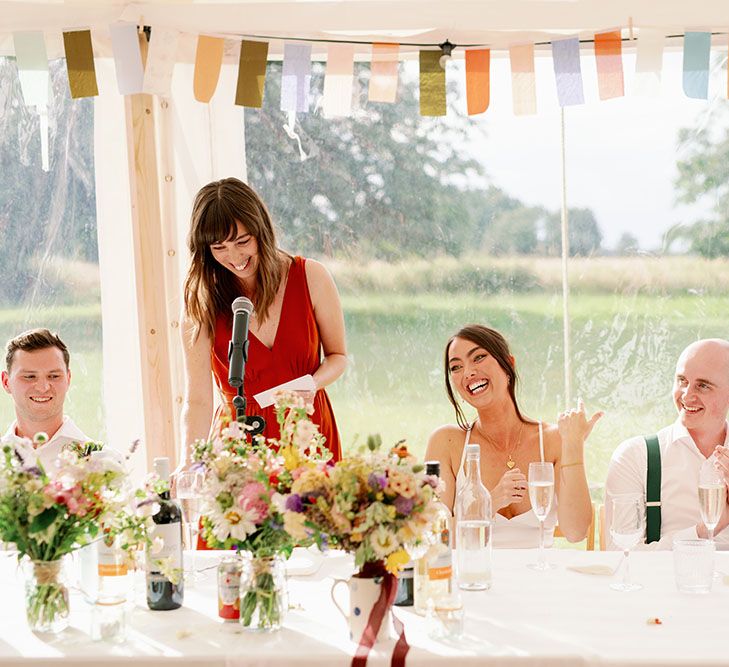 Bride & groom sit at the head table as wedding guests reading speeches during marquee reception 