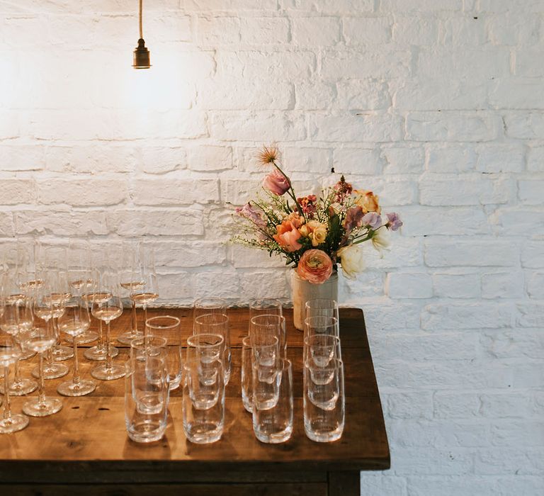 Glasses on wooden table complete with pastel floral bouquet 