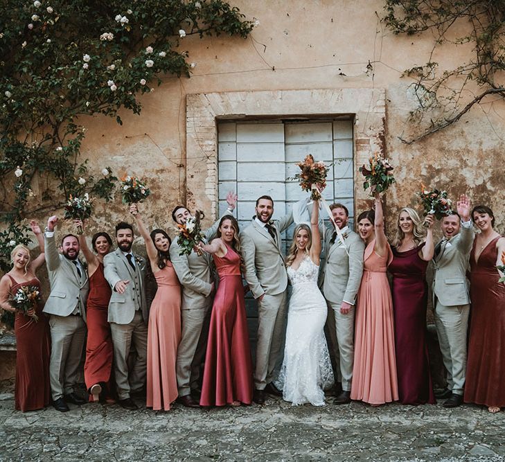 Bride & groom stand with their wedding party and bridesmaids wearing terracotta orange dresses in different styles and fabrics  