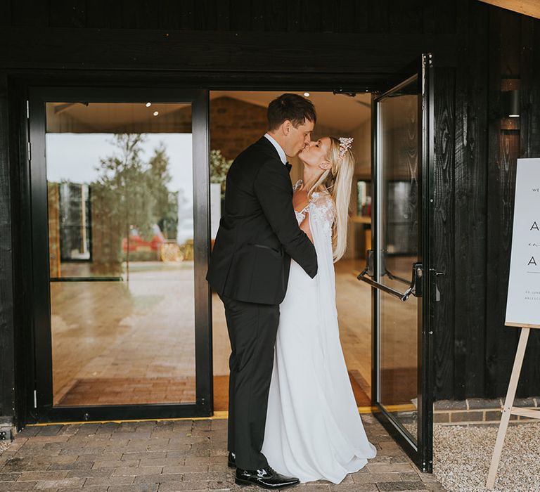 Bride and groom share a kiss next to their welcome wedding sign 