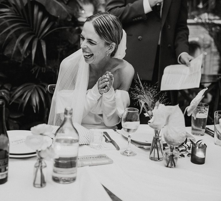 Bride laughing as the groom reads out his speech