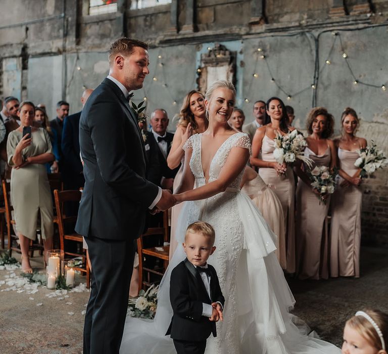 Bride & groom hold hands as their son stands with them at the altar for ceremony at The Asylum 