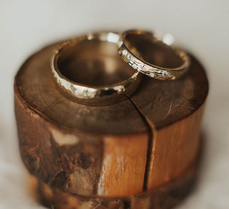 Gold wedding band with another gold wedding band with diamonds inlaid on a tree slice 