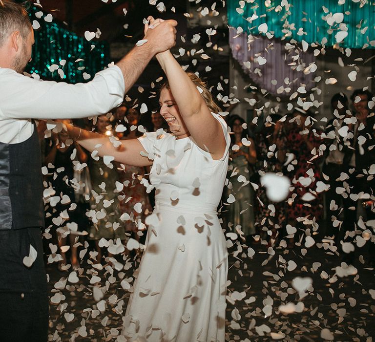 Bride and groom share their first dance as white confetti falls over them 