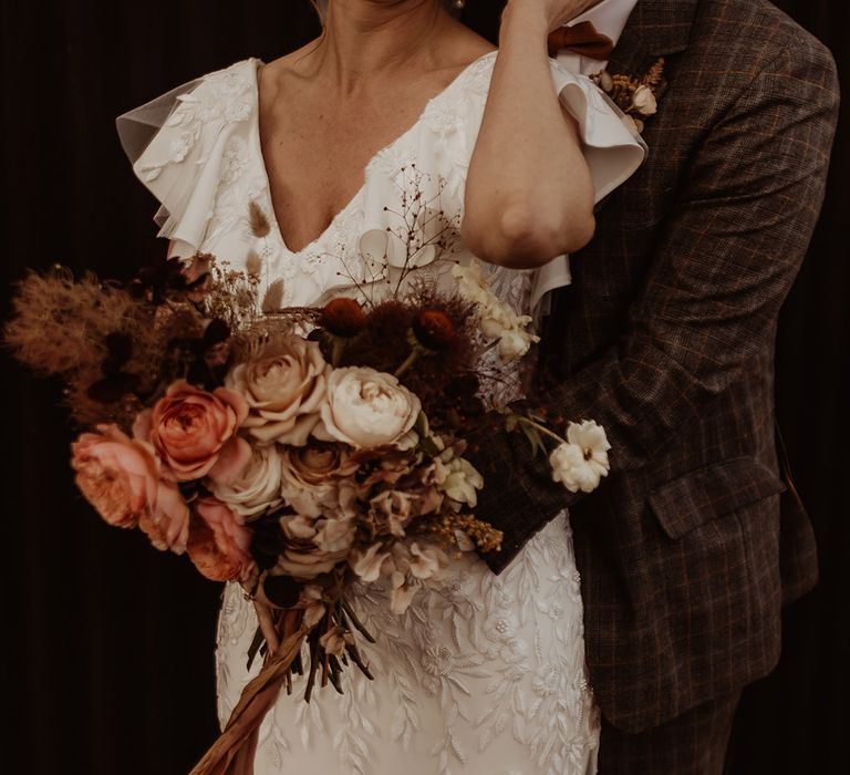 Bride in a bespoke Emma Beaumont Atelier wedding dress with embroidery and beads with the groom in a grey suit and a pink and white bouquet 