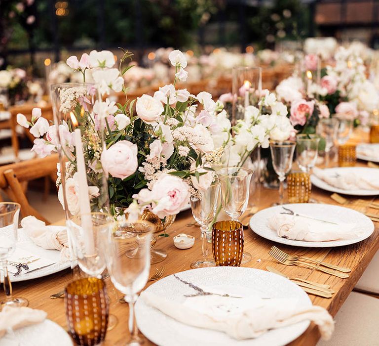 Pink and white wedding flowers, gold cutlery, pink napkins for a classic tablescape in a glass marquee 