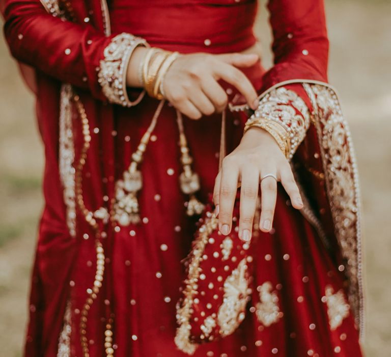 Bride wears neutral nail colour and gold bangles with her long sleeved red bridal separate with gold embellishment 