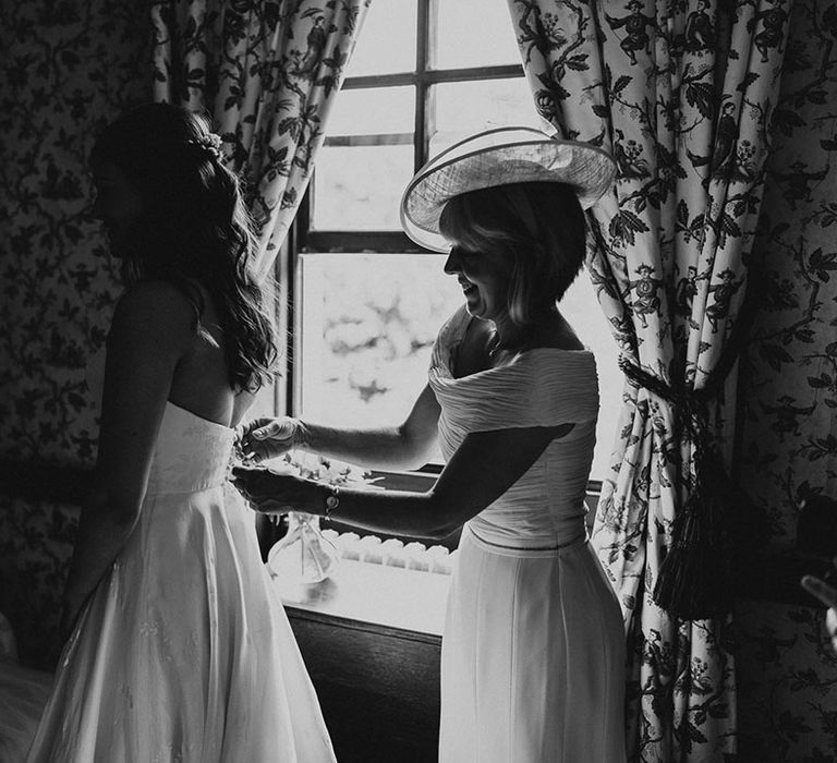 Mother of the bride in an off the shoulder white gown helps the bride into her Phillipa Lepley strapless wedding dress 