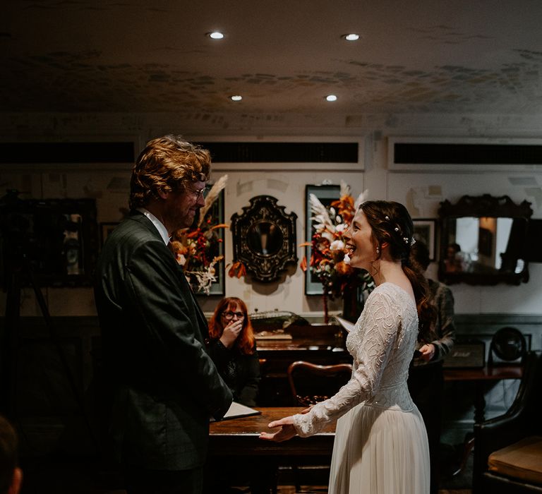 Groom in dark suit with orange tie and autumnal boutonniere and bride in long sleeve lace vintage wedding dress and closed toe satin heels holding hands at the alter 