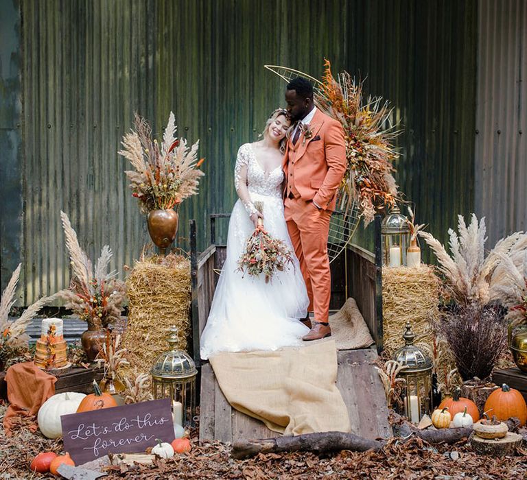 Bride and groom standing on the back of a wooden trailer with giant gold crescent moon ceremony backdrop, rustic props, copper and stoneware with everlasting dried flower arrangements.