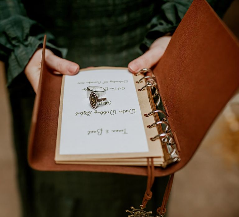 Celebrant in forest green tartan dress holding tan Filofax with wedding vows and chunky boho wedding rings 