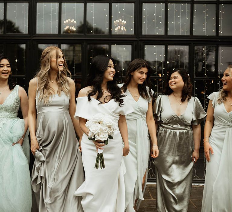 The bridesmaids wear mismatched sage green bridesmaid dresses walking alongside the bride for fun bridal party shots 