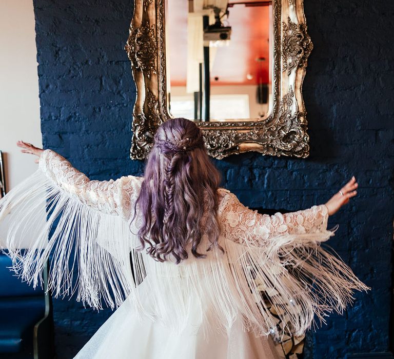 Bride in midi-length bridal gown with lace embroidered sleeves and large white fringing along the sleeves and polka dot wedding boots twirling around 