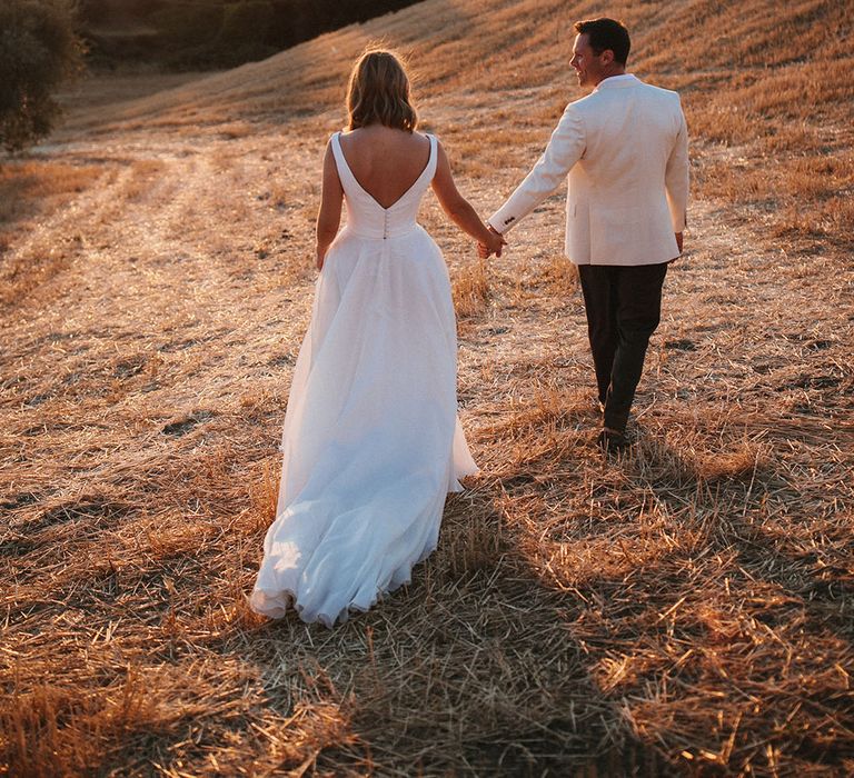 Bride & groom walk through the Tuscan countryside during golden hour 