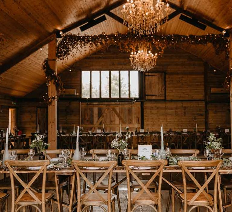 High Billinghurst Farm reception room with artistic hanging chandeliers, fairy lights, tapered candles in painted wine bottles decor and foliage centrepieces 