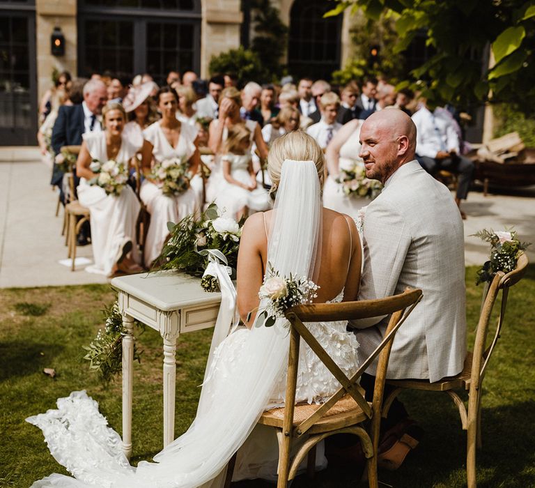 The bride and groom sit together and sign the wedding register with their guests watching them