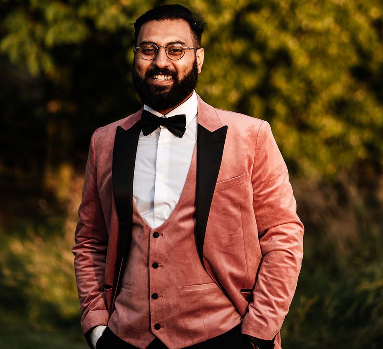 Groom in pink velvet three piece tuxedo with black bow tie 