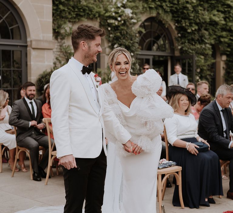 Groom in white tuxedo with the bride wearing statement puff sleeves at romantic outdoor wedding 