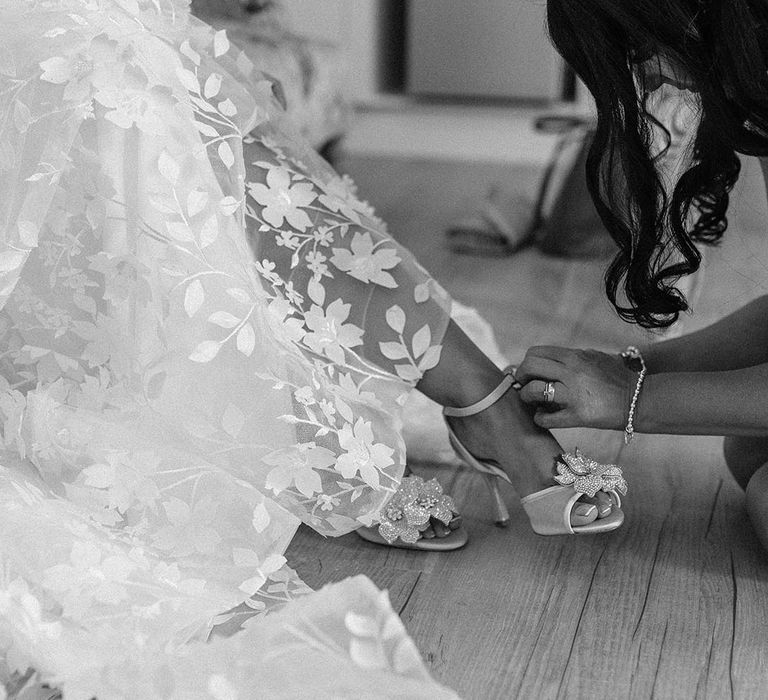 Bridesmaid helps the bride into her sparkly floral silver wedding shoes 