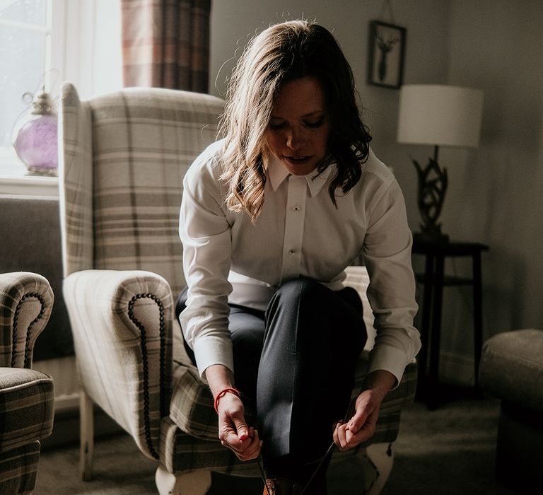 bride on the wedding morning in a navy suit putting on brown brogue boots 