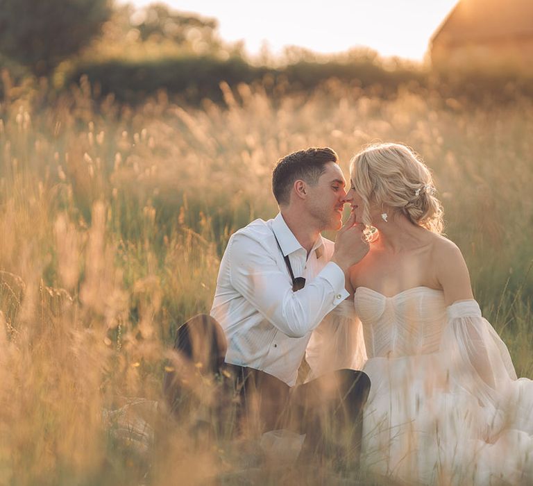 Bride and groom sitting in a field kissing at oxfordshire wedding