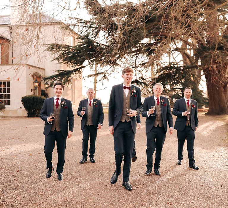 Festive red wine being held by groom and groomsmen in navy suits with grey and red details 