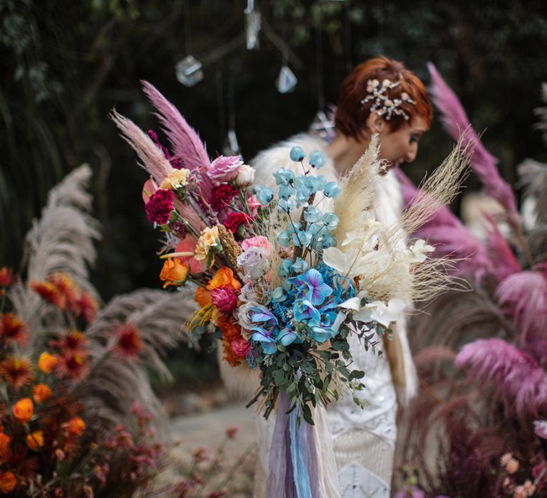 Bride carrying oversized bouquet with pink, orange and blue wedding flowers in sparkly white wedding dress 