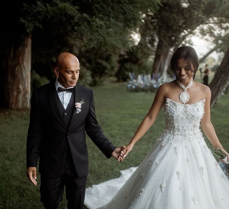 Bride in pearl wedding dress walking with the groom for the wedding couple portraits 