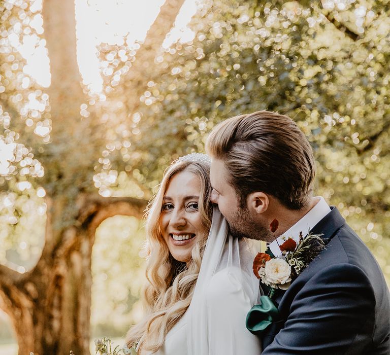 The groom in a three piece suit hugs the bride from behind at the wedding for couple portrait 