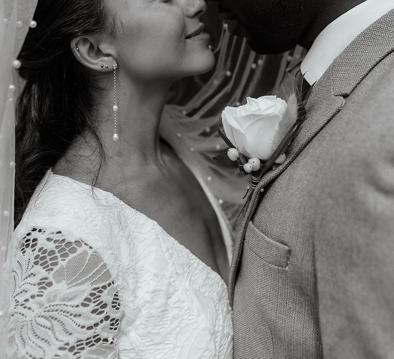 The bride and groom share a kiss underneath the pearl embellished wedding veil 