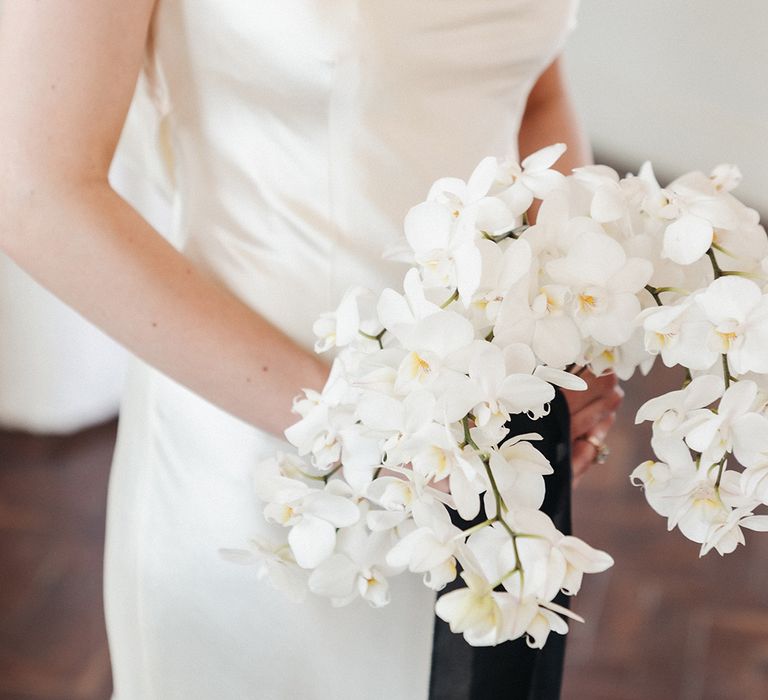 Bride holding all white wedding bouquet with orchids tied with black ribbon 