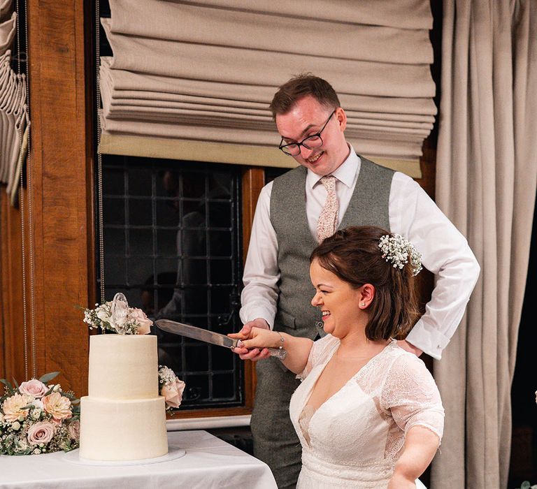 Two tier white wedding cake being cut by the bride and groom at their classic wedding 