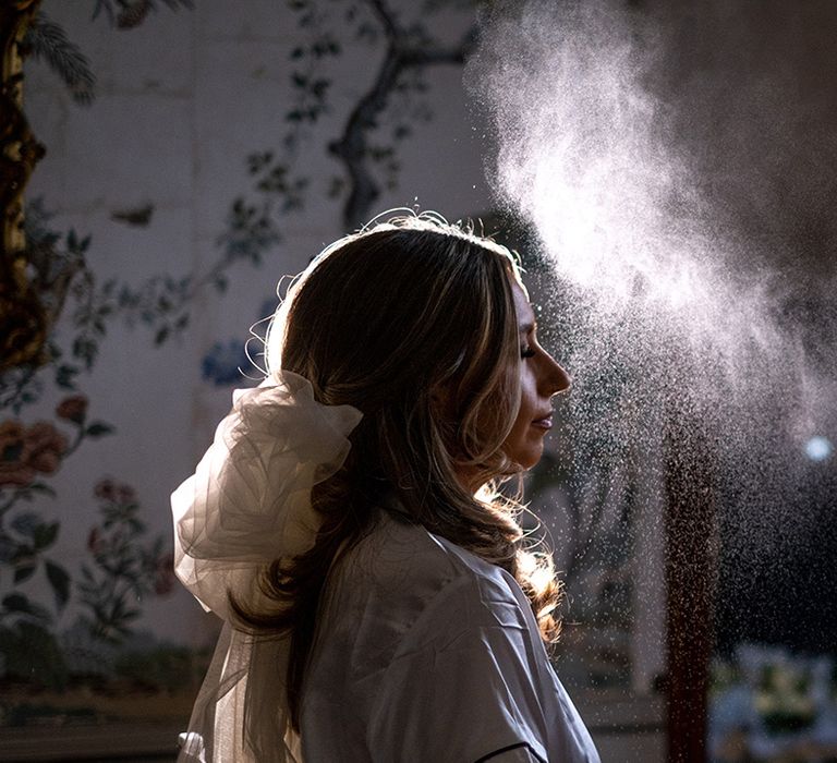 Makeup artist sprays setting spray over the bride to keep her makeup in place 