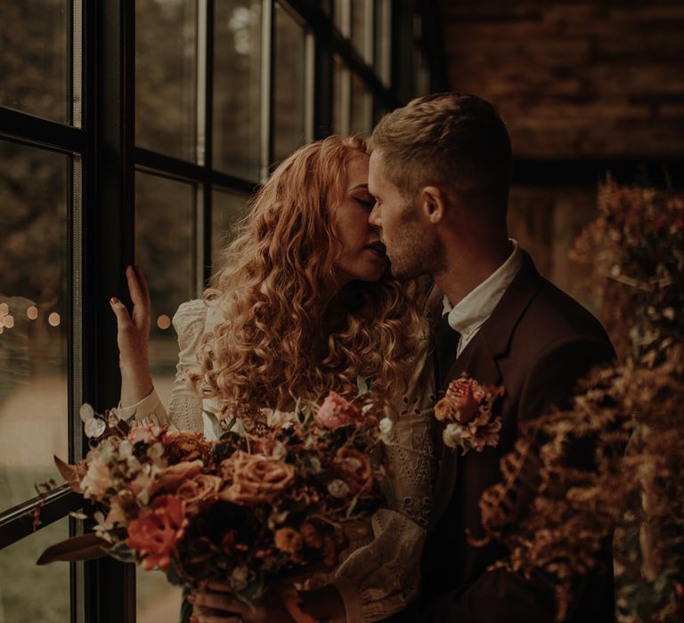 Groom in burgundy suit kissing his bride