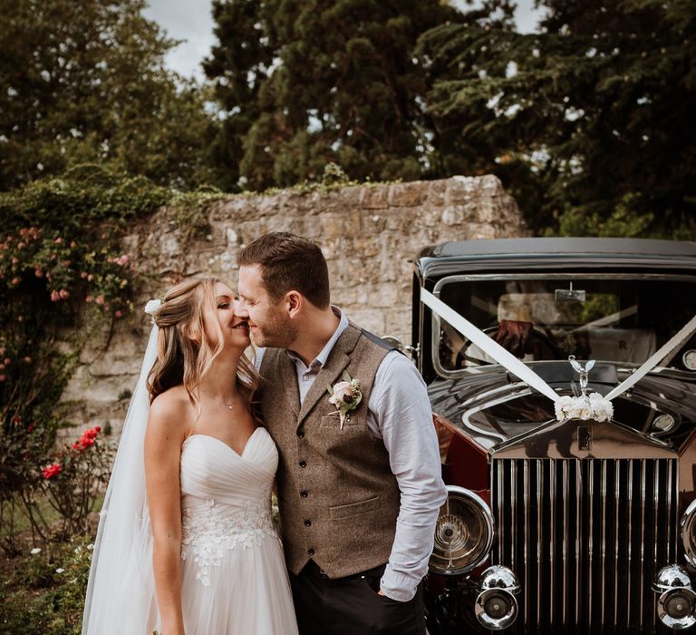 Bride in blush strapless wedding dress kissing her groom by the vintage wedding car 