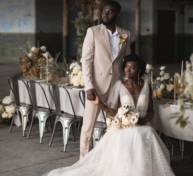 Bride in Berta wedding dress sitting at the reception table holding her grooms hands in a beige suit 