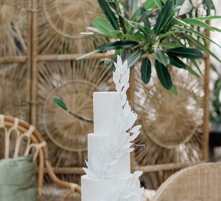 White three-tier textured wedding cake on glass stand with leaf detail