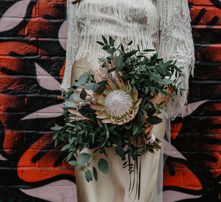 Bride holding large protea bouquet stands again vibrant graffiti wall