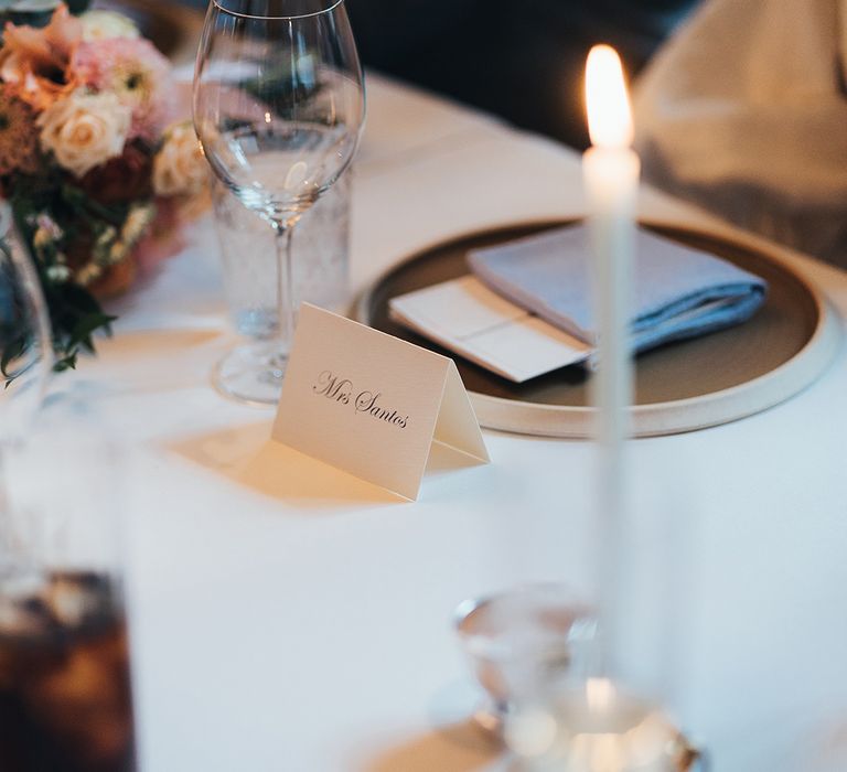 Wedding tablescape with white candles, pink floral bouquet, white name place setting and wine glasses 