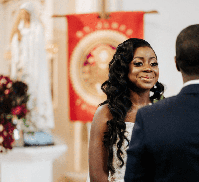 A bride with waist length curly hair smiles during her wedding ceremony.