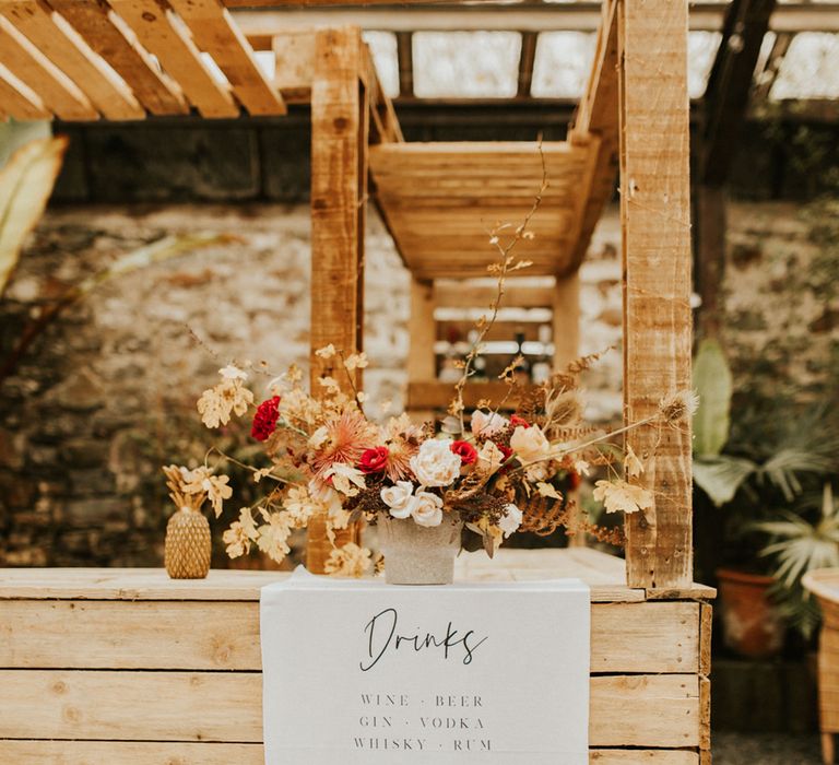 Wooden barn decorated with a script drinks menu and autumn wedding flower arrangement 