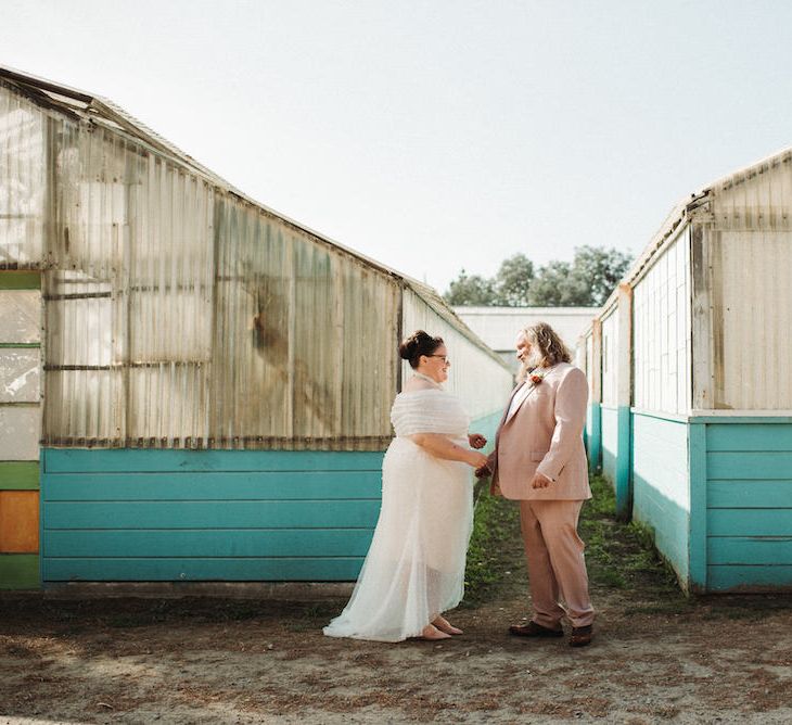 Bride in an off the shoulder wedding dress with pearl detail and groom in a pink suit at first look 