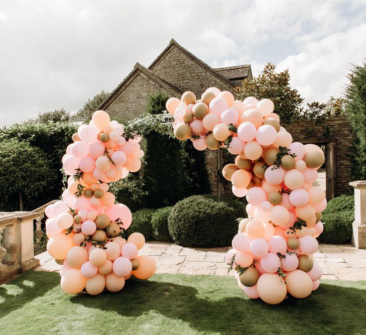 Pastel pink and gold balloon arch with vines on the lawn at Euridge Manor wedding