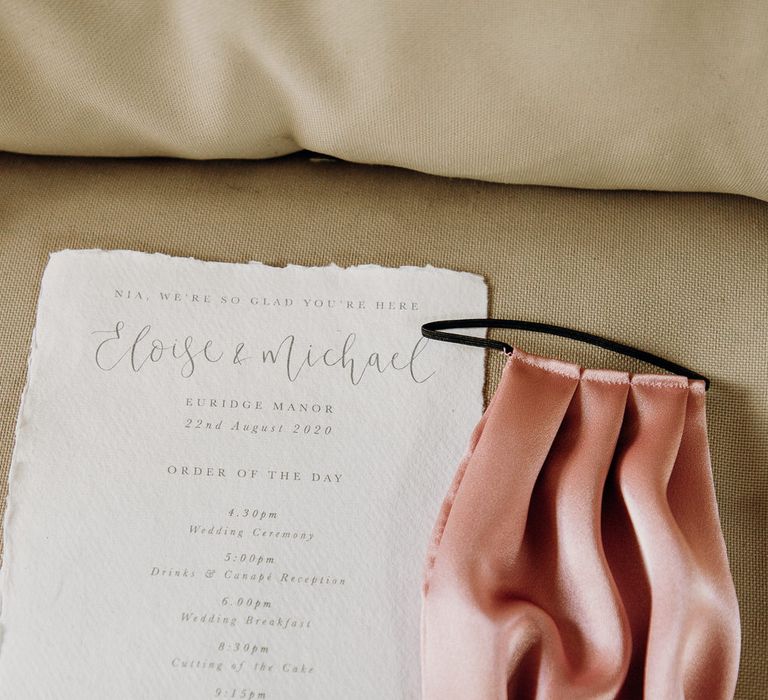 Silk blush pink face mask and order of service on white parchment paper by Lou Paper