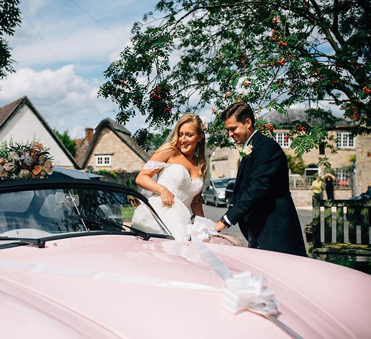 Groom helping his new wife get into pink porsche