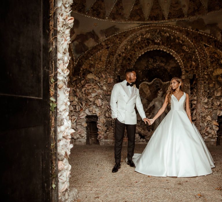 Groom in a white double breasted jacket holding hands with his bride in a princes Justin Alexander wedding dress 