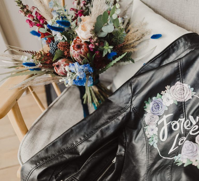 A personalised leather jacket by The Mermaid Effect next to a bright bouquet of red and blue flowers