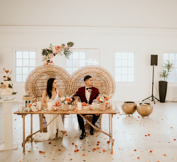 Bride and groom sitting on peacock chairs at their intimate sweetheart table listing to wedding guest speeches 