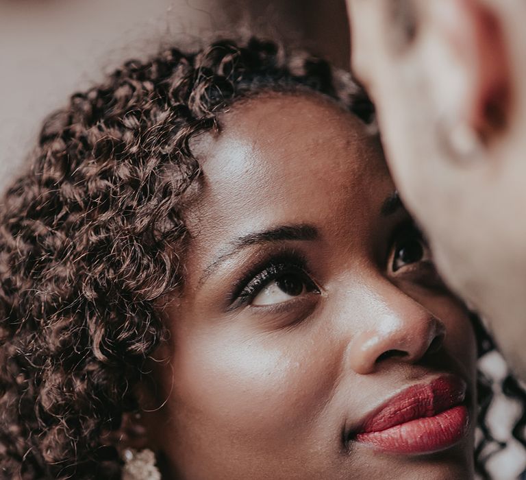 Black bride wearing red lipstick looks lovingly at groom 