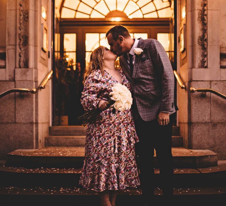 Bride & groom kiss on the steps in front of a brightly lit Chelsea Old Town Hall